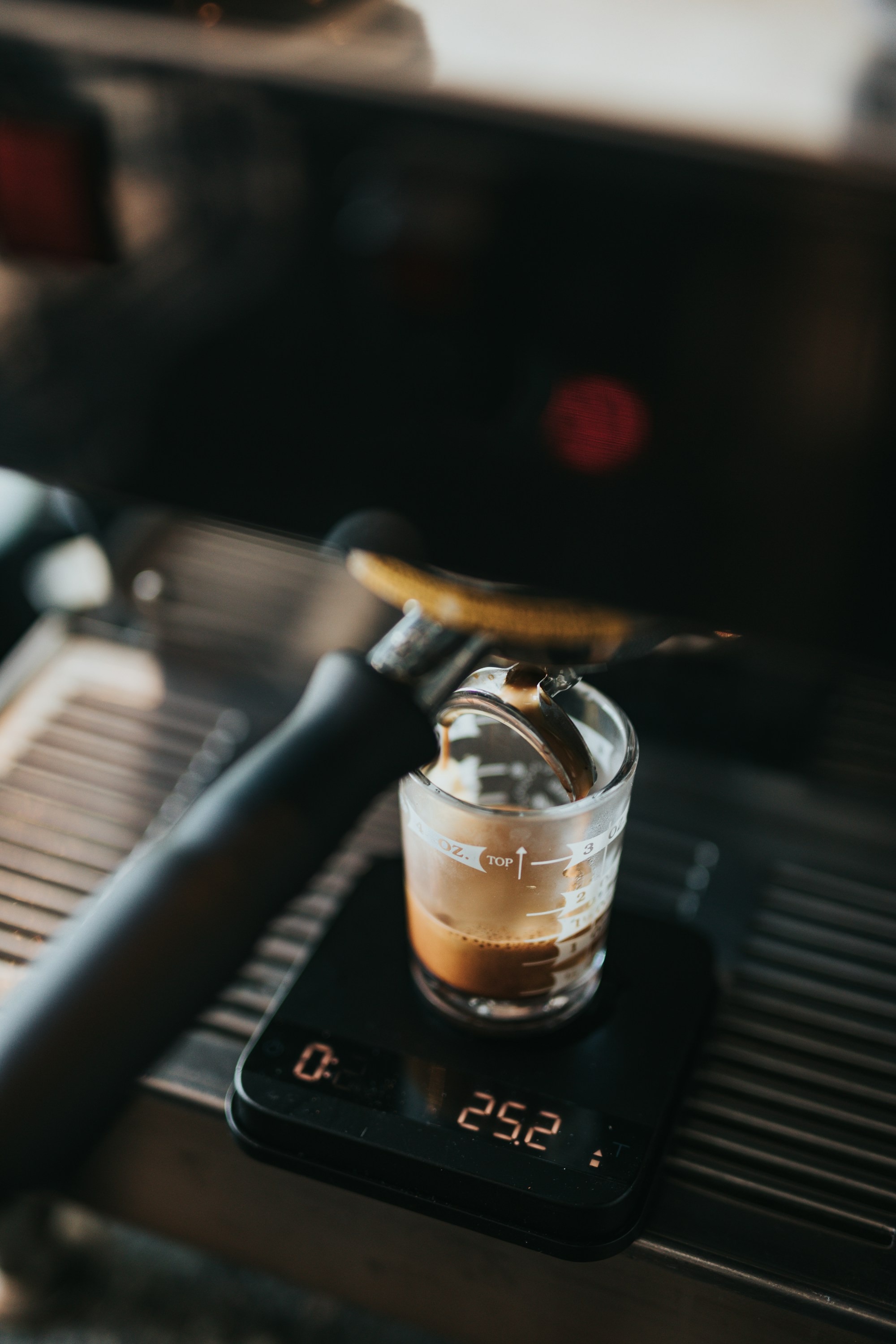 Closeup photo of black espresso maker filling clear glass cup
